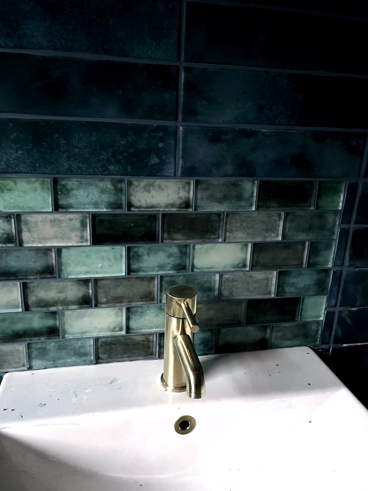 Brushed brass basin tap against glazed green metro tile
